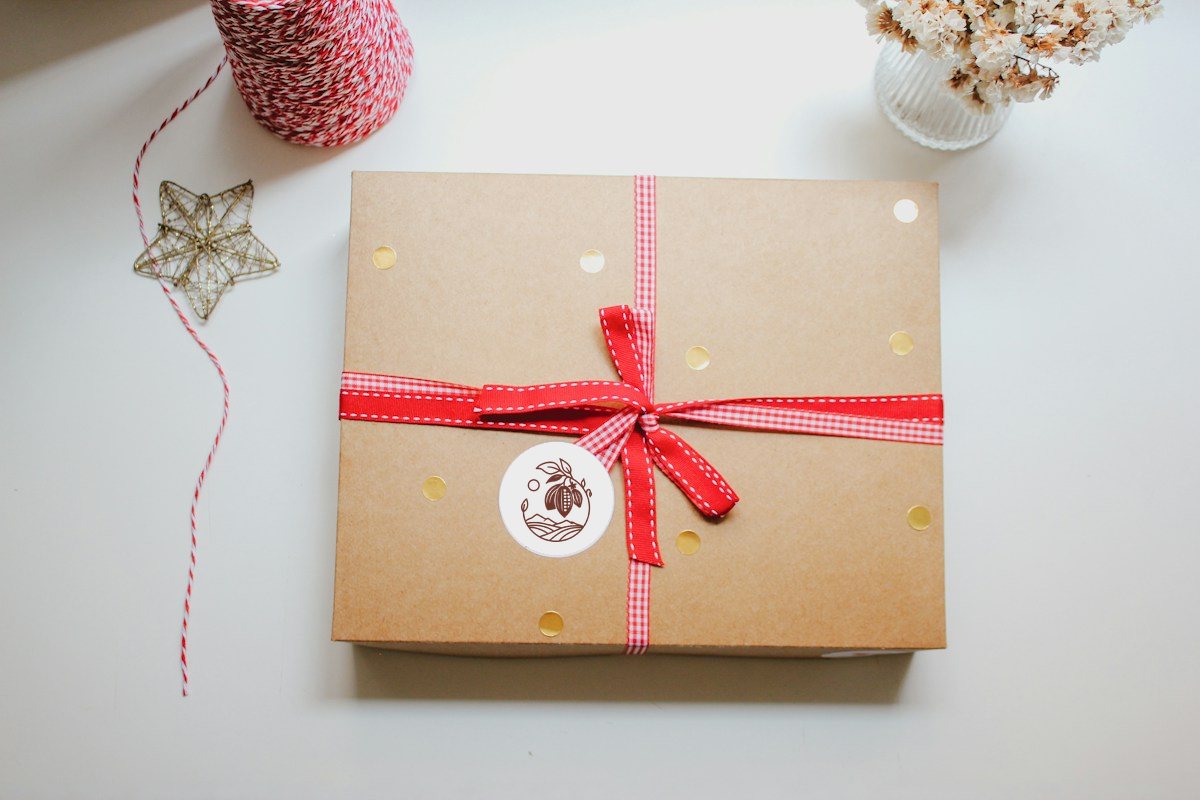 Hộp quà giấy kraft buộc ruy băng đỏ, có nhãn tròn ở giữa